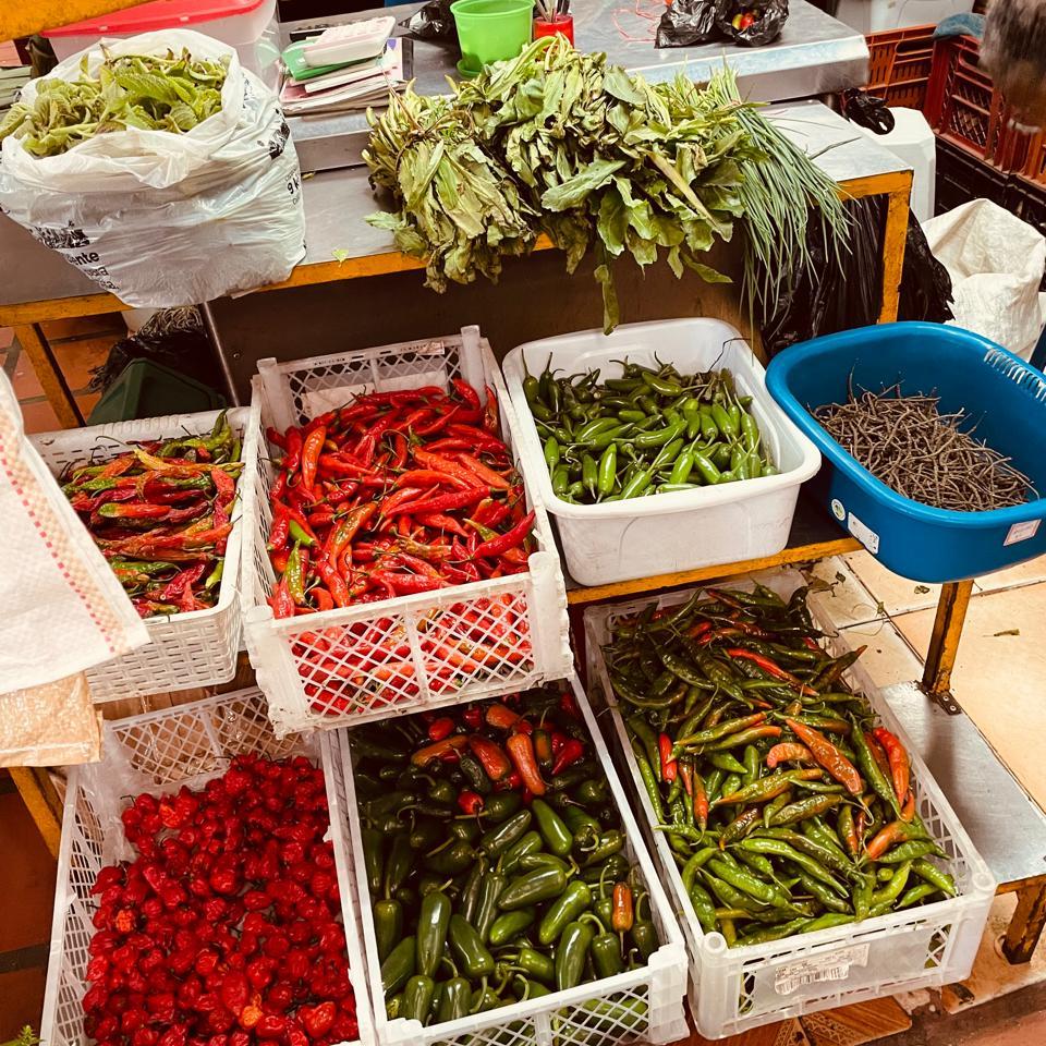 Puesto con diferentes tipos de ajíes, chiles y hierbas frescas en la Plaza Minorista de Medellín, recorrido guiado por Meli Ospina