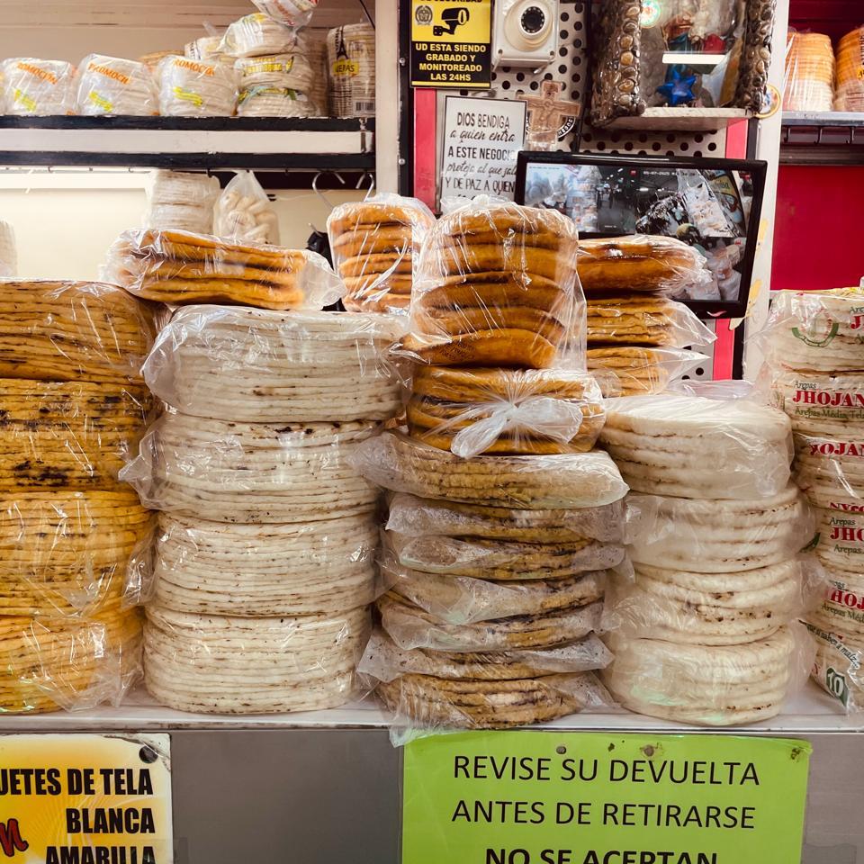 Pilas de arepas blancas y amarillas en un puesto de la Plaza Minorista José María Villa en Medellín
