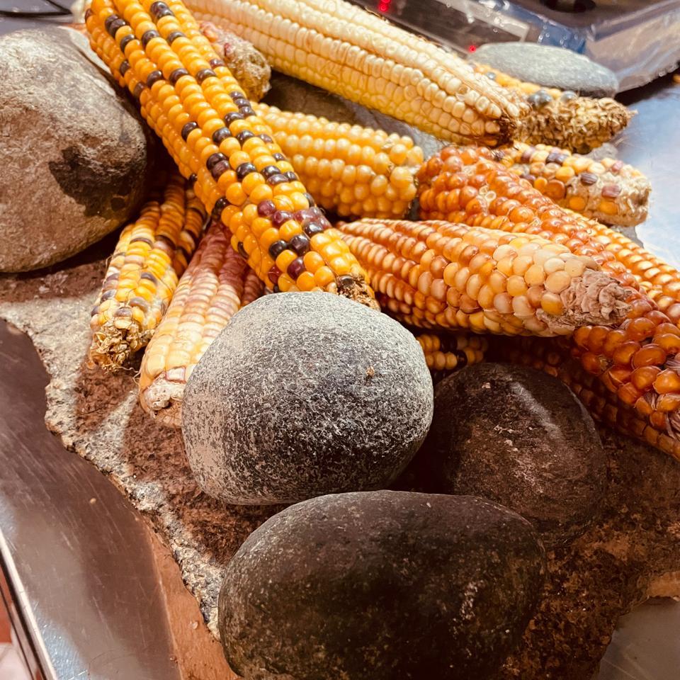 Mazorcas de maíz criollo junto a piedras de molienda en la Plaza Minorista de Medellín, parte del tour gastronómico de Meli Ospina